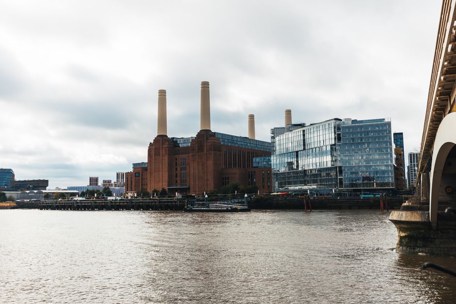 A photograph capturing a house removal process in an urban setting along the riverbank, where a large white moving van with an open side door is positioned next to a multi-storey building. Inside the